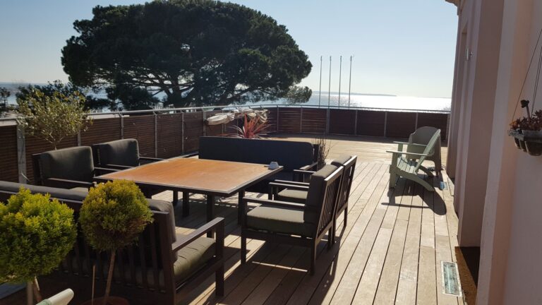 Terrasse en bois meublée face à l'eau : table, fauteuils et bacs plantés