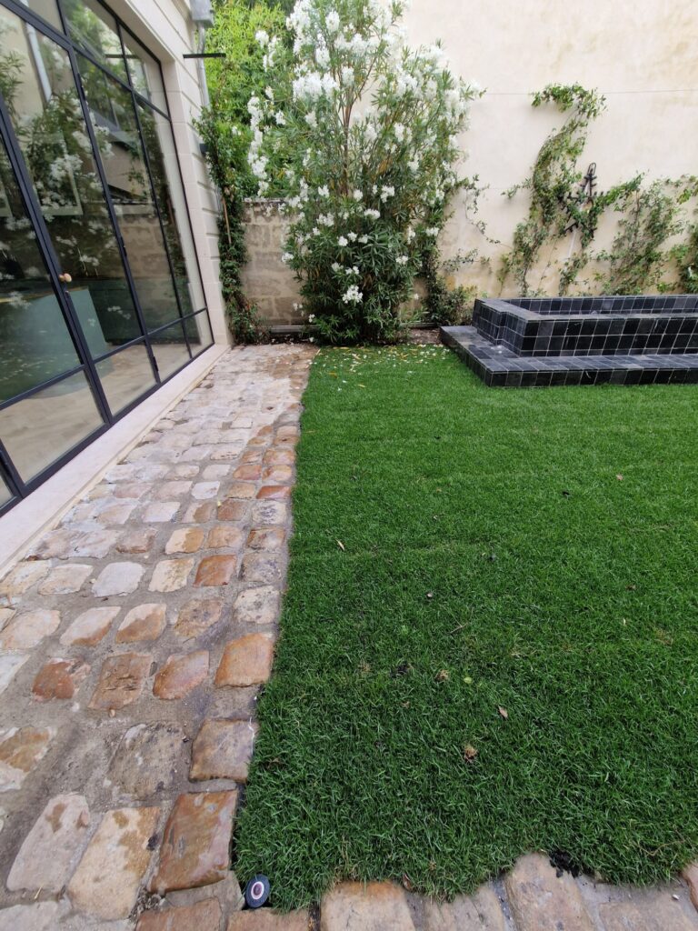 Jardin de ville terminé : gazon, allée pavée et banquette carrelée noire le long de la véranda