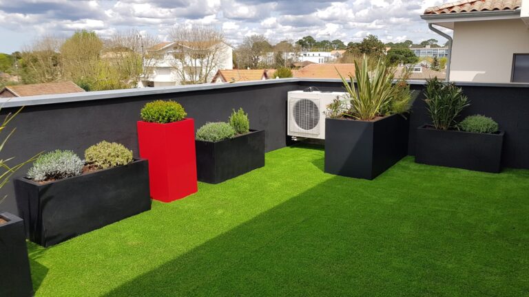 Terrasse aménagée : gazon, bacs noirs plantés de graminées et de lavande, bac rouge et unité de climatisation