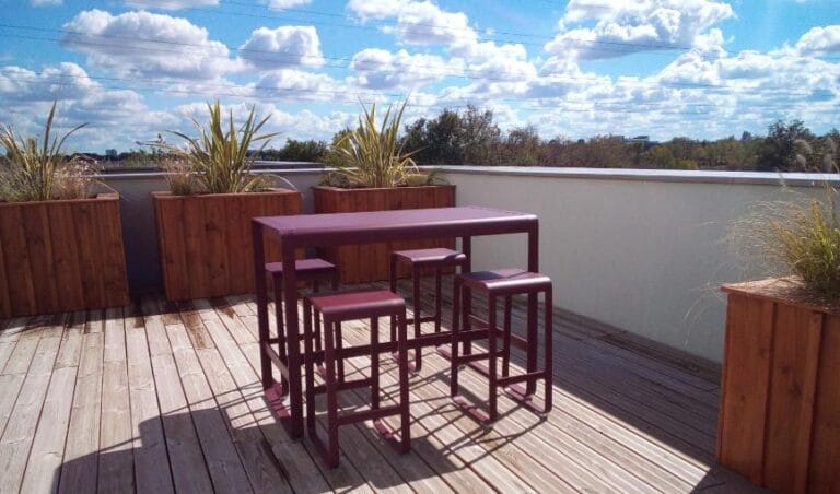 Terrasse d'entreprise en bois avec mange-debout et bacs plantés de graminées