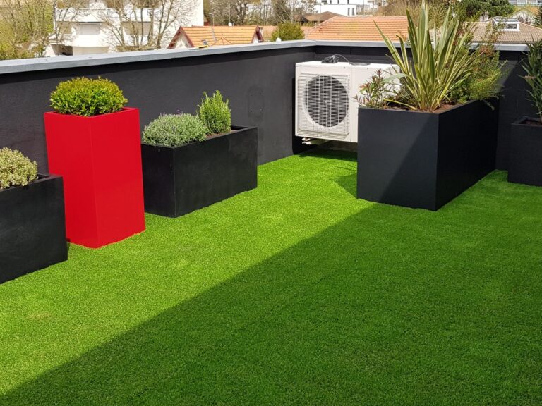 Le même balcon après aménagement : gazon, bacs noirs plantés et bac rouge devant le mur repeint