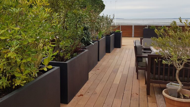 Terrasse en bois neuve après travaux, bacs noirs plantés et mobilier face au bassin