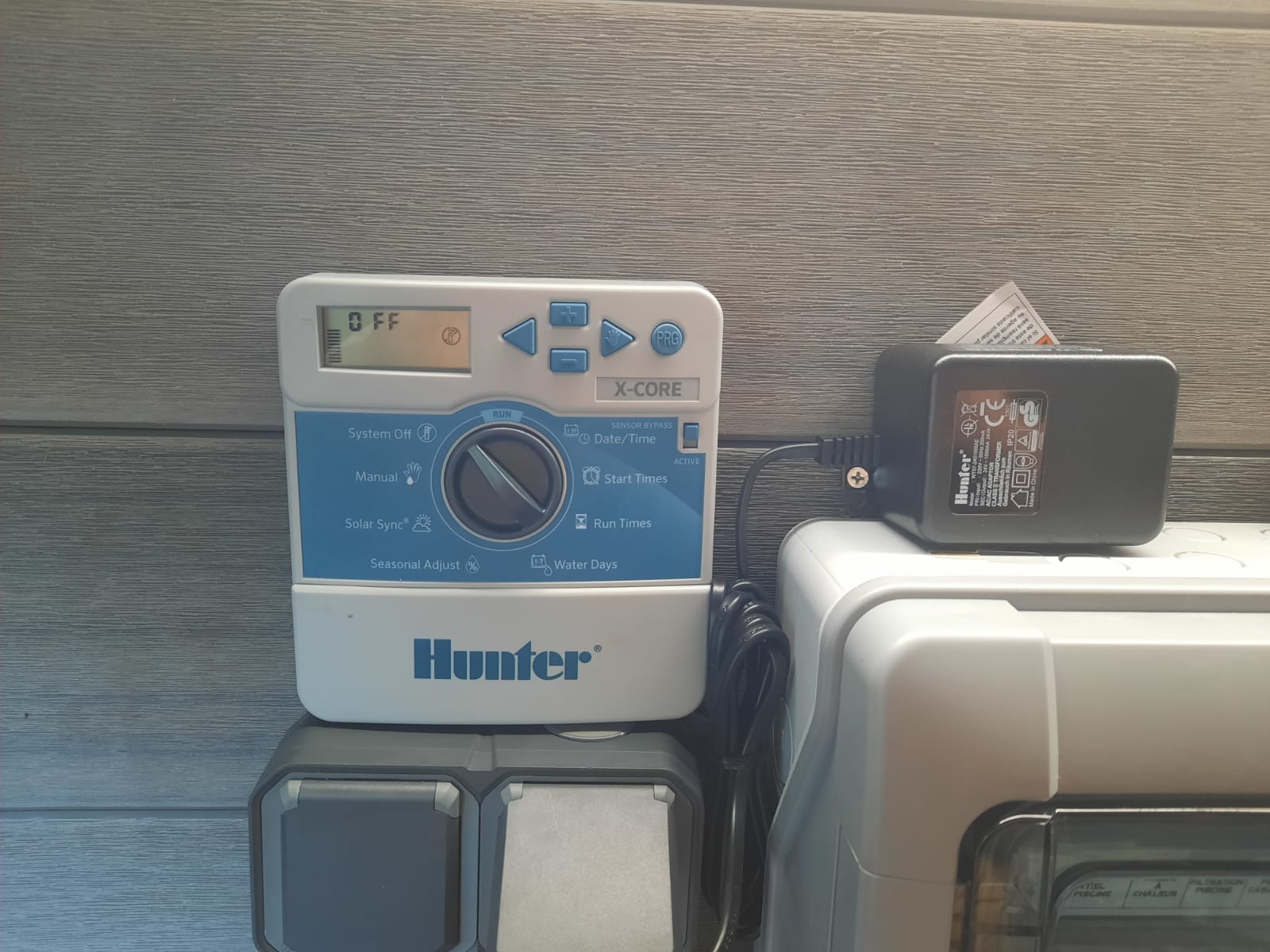 Programmateur d'arrosage Hunter X-Core fixé au mur avec son transformateur, au-dessus des coffrets techniques