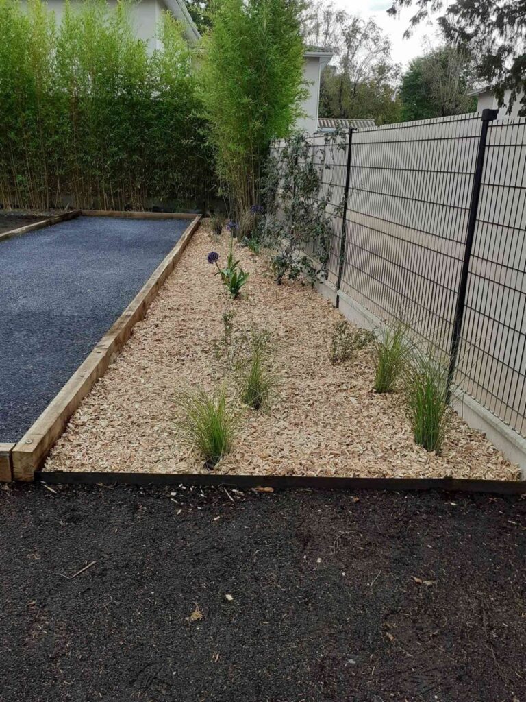 Massif paillé et graminées le long d'un terrain de pétanque